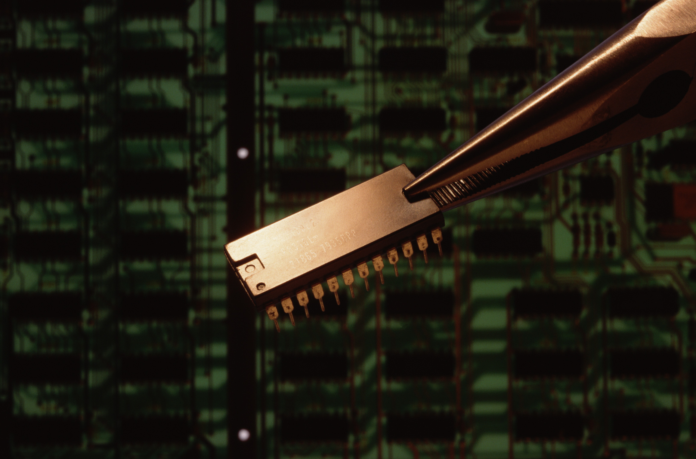 a computer chip, held by tweezers against a black and green background
