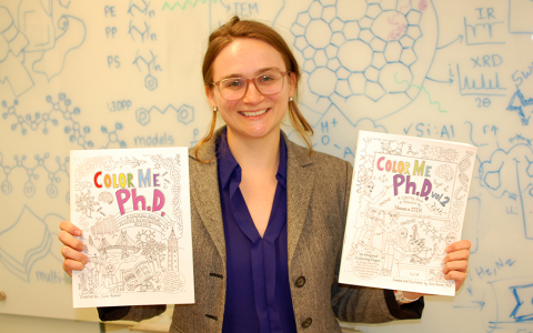 Assistant Professor Julie Rorrer holding copies of her Color Me Ph.D. coloring books
