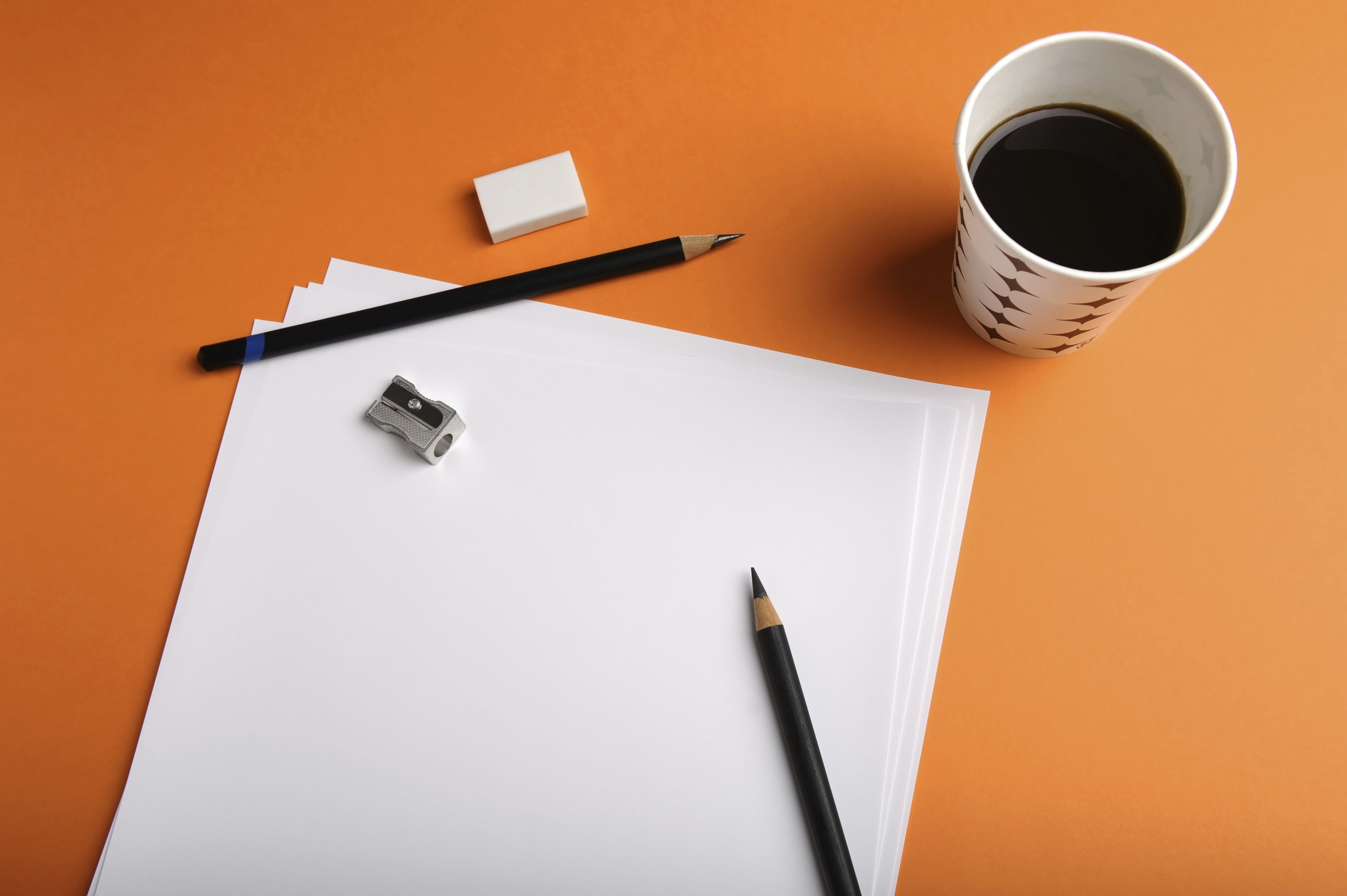 Paper and pencil sit on an orange background next to a full coffee cup