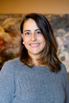 Angela Kimber, a woman with brown, shoulder length hair, smiles at the camera