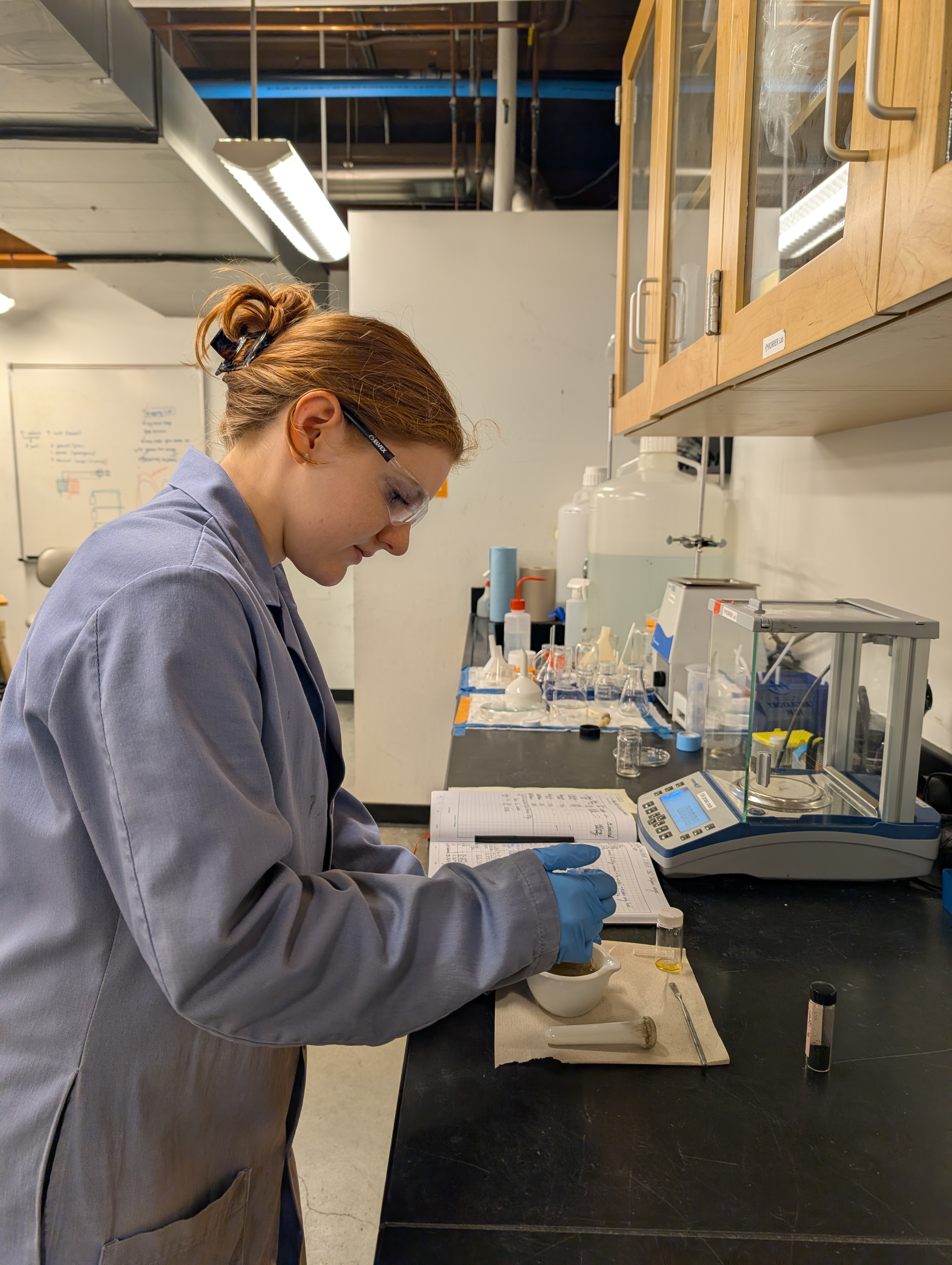 Ellis wears safety glasses and plastic gloves while handling chemicals in the lab.
