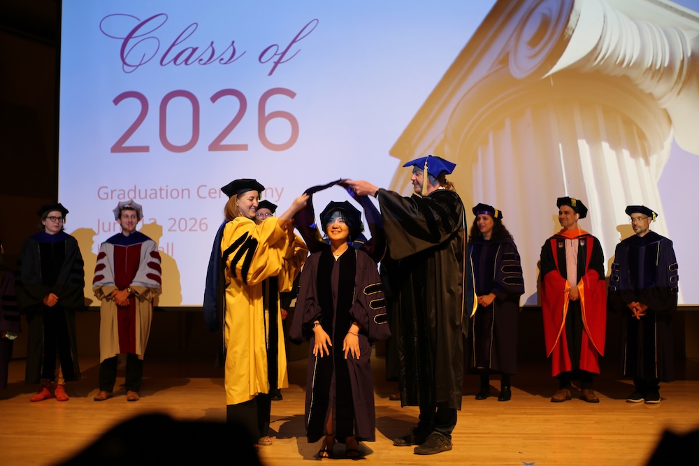 A Ph.D. candidate is hooded by her advisor and the department chair at graduation.