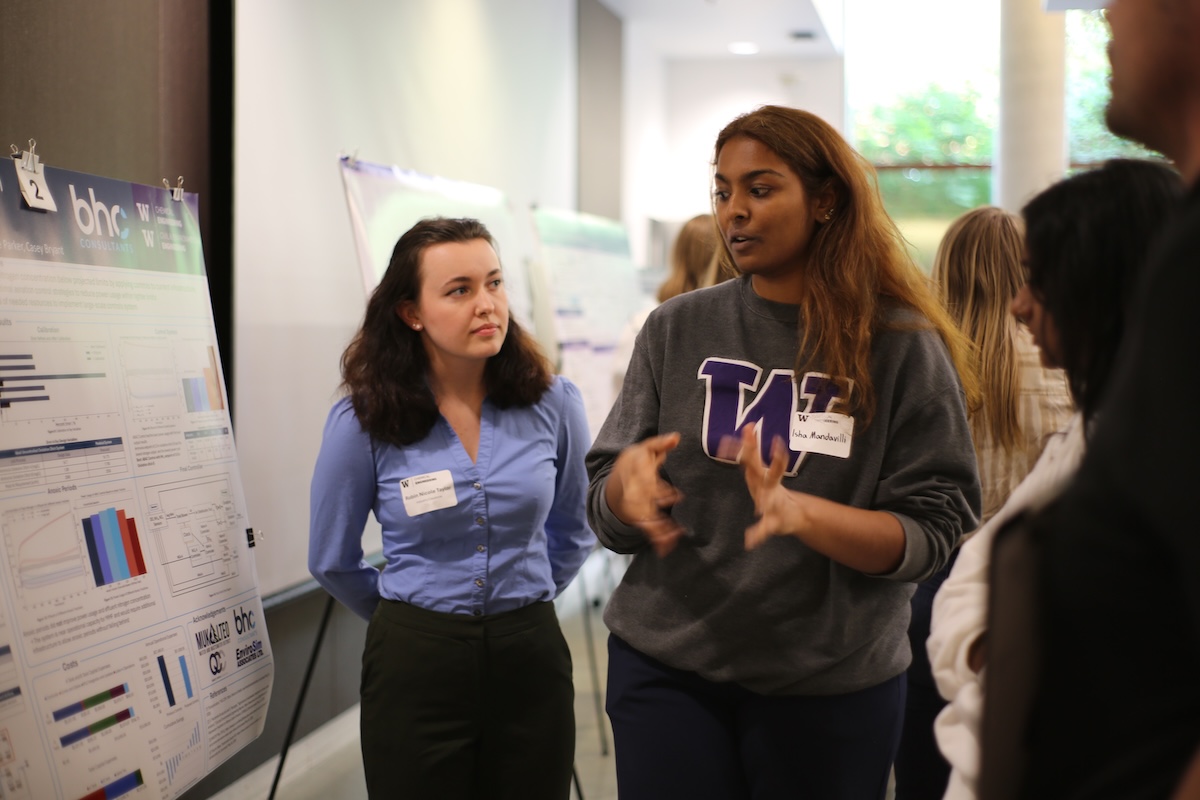 A student explains their research while another student listens.