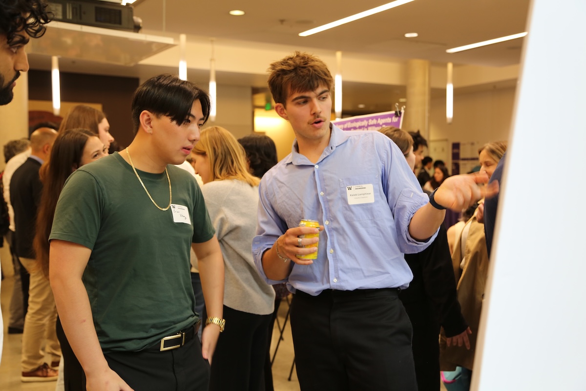 Two students discuss research while gesturing at a poster. 