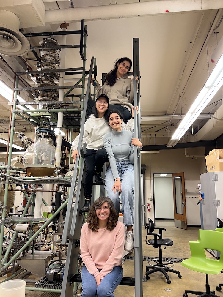 Four people sit on a tall ladder in a lab space.