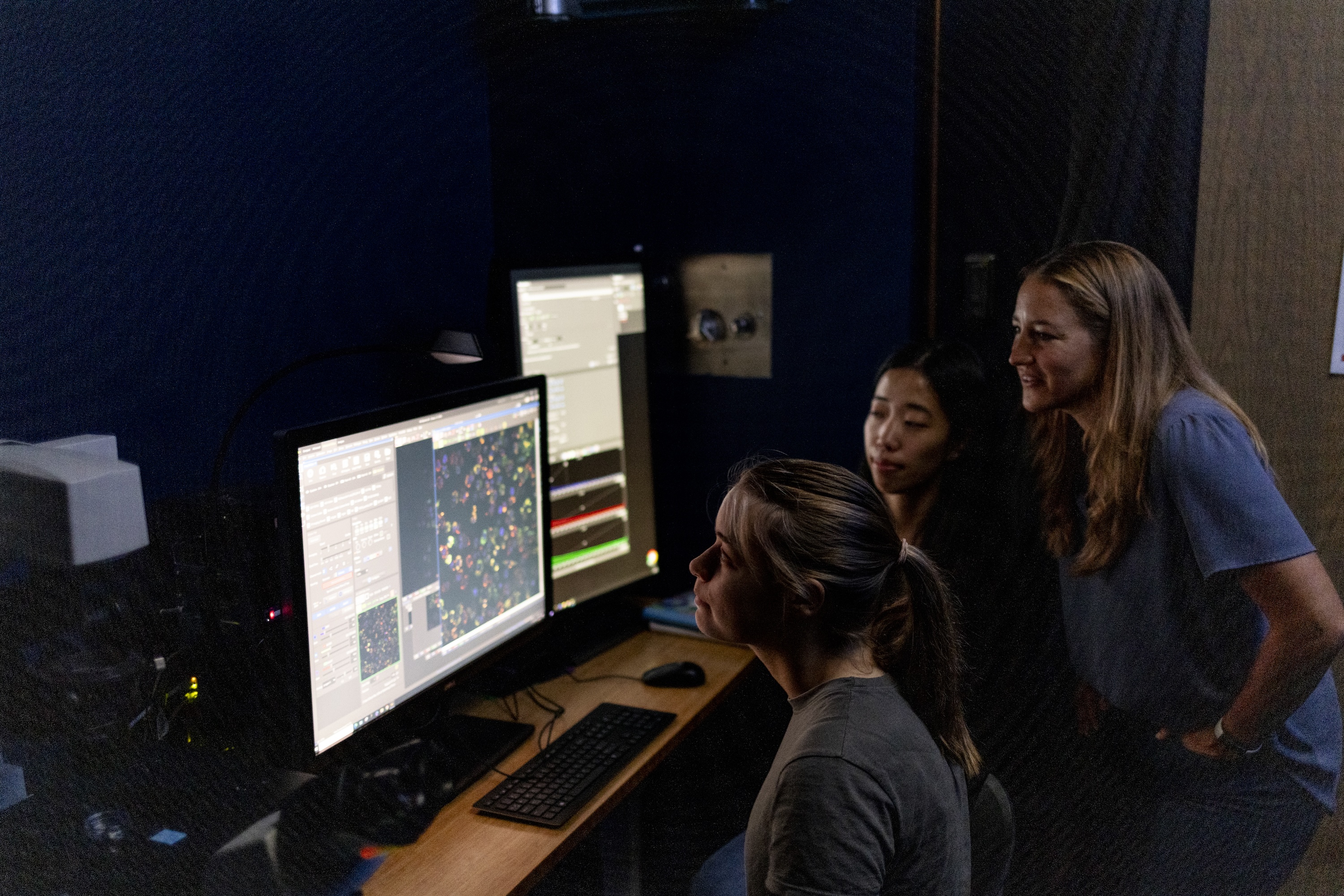 Three researchers gather around a computer screen displaying research results