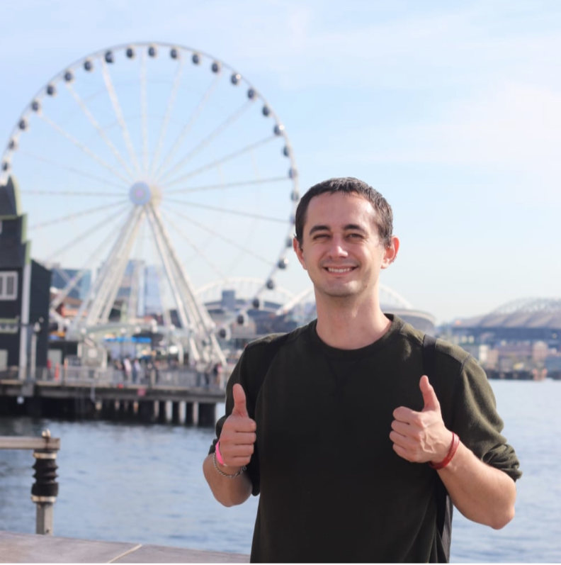 Man giving a thumbs up while standing in front of a ferris wheel