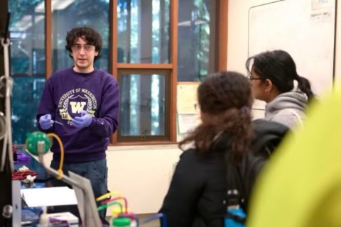 Male student with dark hair and wearing purple sweatshirt presents lab project