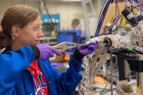Woman in a blue lab coat and safety glasses loads a sample into a reactor in the lab