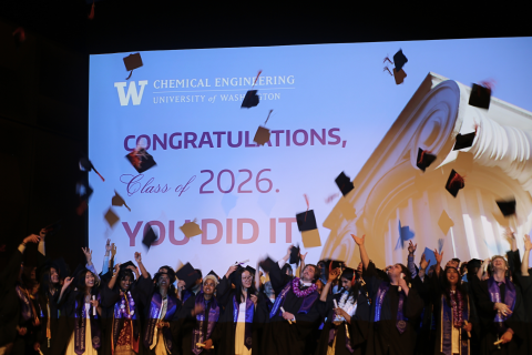 Undergraduate students throw their caps in the air at graduation in front of a slide that says, "Congratulations, class of 2026. You did it!" 