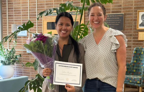 Jullien Berzuela stands with Elizabeth Nance holding a certificate for the Distinguished Staff Awards and a bouquet of flowers. 