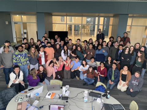 A large group of people sitting in a classroom making silly faces. 