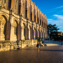A person walking on UW campus in front of the main library on a bright, sunny day. 